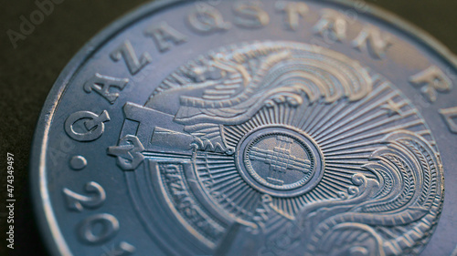 Translation: Kazakhstan. Kazakh 50 tenge coin with the country emblem and focus on shanyrak. Close-up. Blue tinted background or wallpaper for Kazakh economy or state. Macro