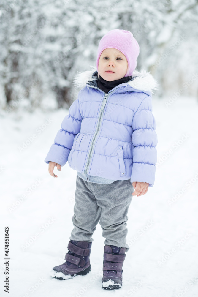 A little girl walks in winter clothes in a snow-covered park.