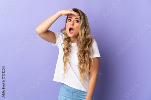 Young Brazilian woman isolated on purple background doing surprise gesture while looking to the side