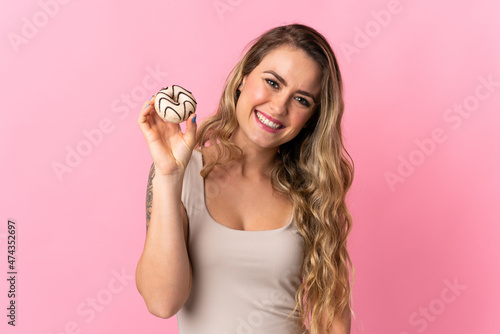 Young Brazilian woman isolated on pink background holding a donut and happy