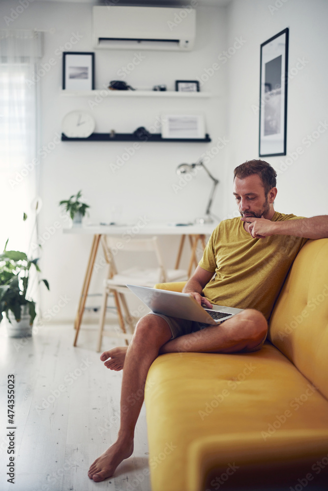 Fototapeta premium Man working on a laptop from the living room. Work from home concept.