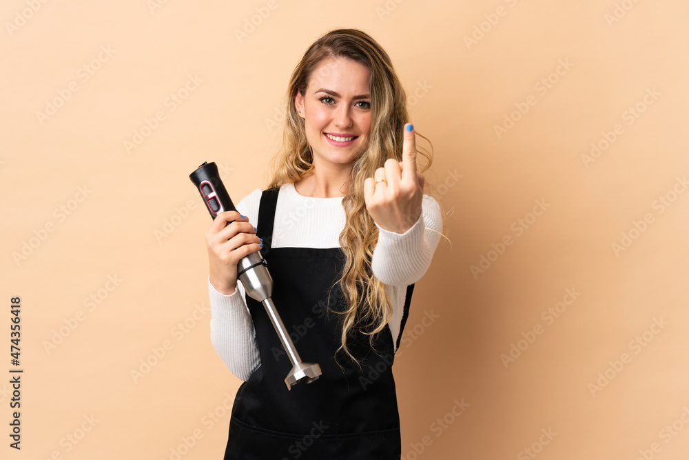Young brazilian woman using hand blender isolated on beige background doing coming gesture Young brazilian woman using hand blender isolated on beige background doing coming gesture