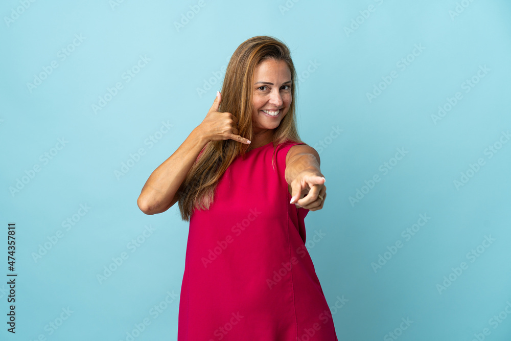 Middle age brazilian woman isolated on blue background making phone gesture and pointing front Middle age brazilian woman isolated on blue background making phone gesture and pointing front