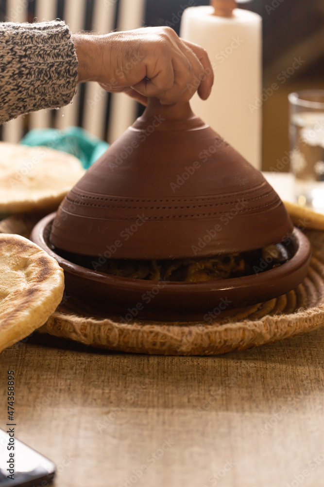 hand uncovering Moroccan tajine on a table