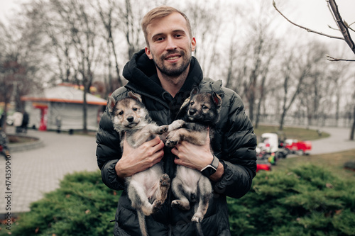 Young man holds two small puppies in his arms.