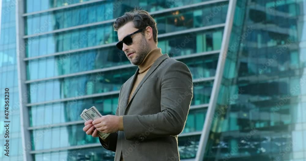 Handsome middle age man holding bunch of usa banknotes smiling happy pointing with hand and finger. businessman in a classic brown suit holds dollar bills in his hand and looks into the camera Handsome middle age man holding bunch of usa banknotes smiling happy pointing with hand and finger. businessman in a classic brown suit holds dollar bills in his hand and looks into the camera