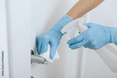 Cleaning black door handle with an antiseptic wet wipe, blue gloves and sanitizer. Sanitize surfaces prevention in hospital and public spaces against corona virus. Woman hand using towel for cleaning.