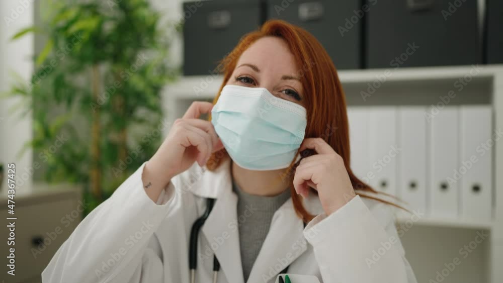 Young redhead woman wearing doctor uniform and medical mask working at clinic Young redhead woman wearing doctor uniform and medical mask working at clinic