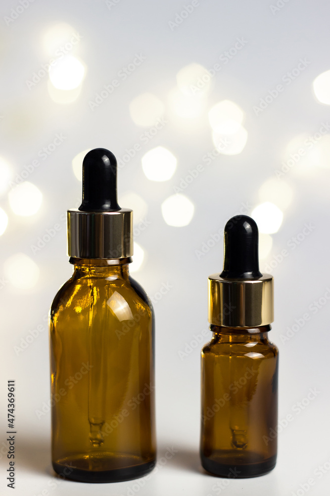 White background with warm yellow round bokeh. Copyspace. New Year's holiday lights. Christmas. Glass brown cosmetic jars with a pipette. Artificial Christmas tree. White background with warm yellow round bokeh. Copyspace. New Year's holiday lights. Christmas. Glass brown cosmetic jars with a pipette. Artificial Christmas tree.