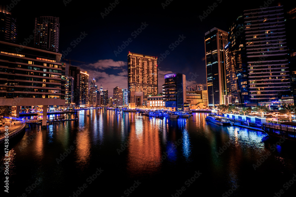 Obraz premium Scenic long exposure night view of the Dubai Marina with it's tall skyscrapers raising next to the yacht marinas and waterfront, Dubai, UAE