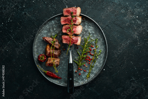 grilled marbled beef steaks striploin on a fork. On a black stone background.