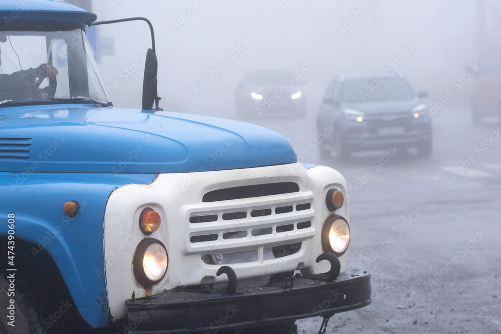 Naklejka premium Fog on the road. An old truck drives into a city crossroads.