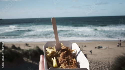 POV of a hand holding a box of Fish and Chips at Fistral Beach, Newquay, Cornwall on a sunny day. photo