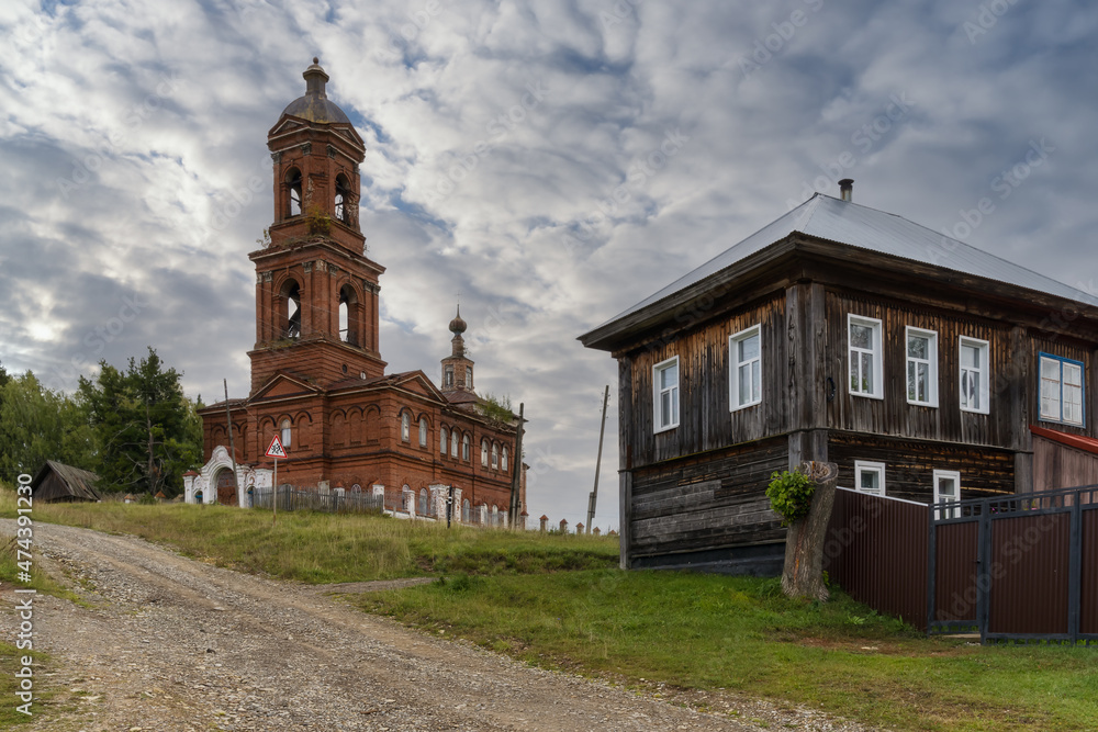 View of an old dilapidated brick church with a bell tower on a high hill on a sunny summer day in the village of Vilgort (Northern Ural, Russia). Wonderful historic architecture. Around wooden houses 