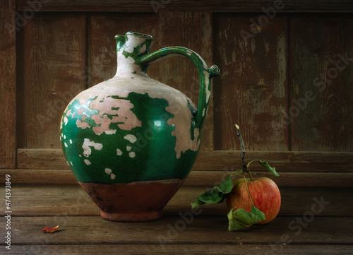 A ripe apple with fresh leaves just plucked from a tree and an old peeling ceramic jug. photo