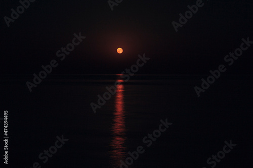 The Full Red Moon Shines Brightly in the Sky on a Dark Night Over the Calm Sea. Beautiful Moon Path on the Water photo