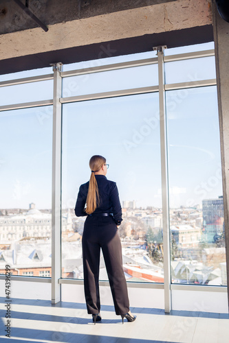 Confident business woman boss standing in modern office or hotel window enjoying big city view, woman leader, business owner thinking about future success, planning new opportunities,