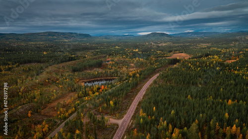 Landscape with Wildernes Road through forest in autumn in Lapland in Sweden from above, colored trees and clouds in sky.