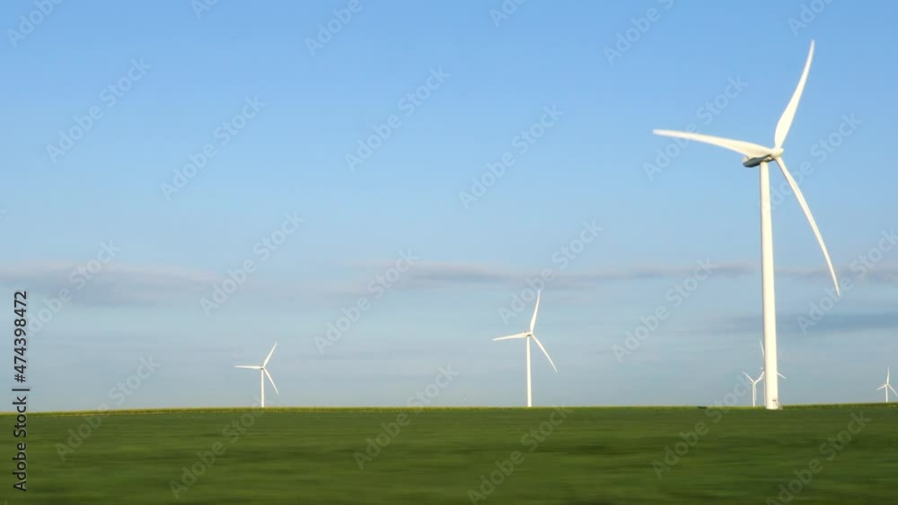 Wind turbine in a green field; tracking past turning white turbines with clear blue sky on early summer morning. 216B Wind turbine in a green field; tracking past turning white turbines with clear blue sky on early summer morning. 216B