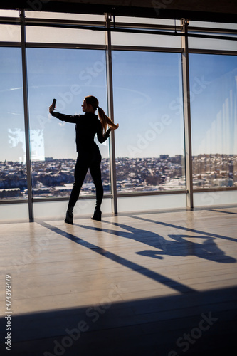 A beautiful girl takes a selfie on her phone against the background of panoramic windows in a skyscraper