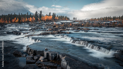 Trappstegsforsen waterfall in autumn along the Wilderness Road in Lapland in Sweden, clouds in the sky. photo