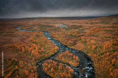 River with colourful trees in the countryside of Lapland at Stokenjokk Plateau in autumn in Sweden, from above with dark clouds.