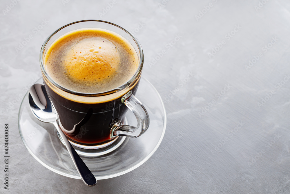 Americano coffee on a gray background. Morning coffee in glass cup. Transparent cup of coffee on a transparent saucer. Copy space Americano coffee on a gray background. Morning coffee in glass cup. Transparent cup of coffee on a transparent saucer. Copy space