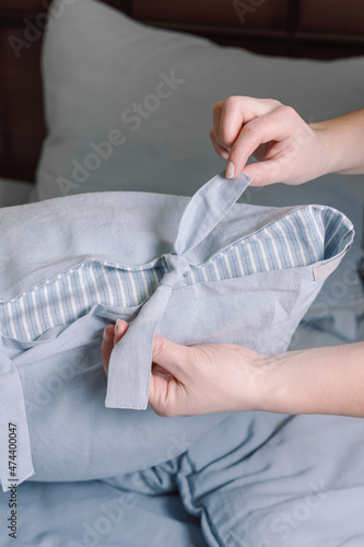 Blue bed linen made of boiled cotton. Bedroom. Woman ties the strings on pillowcase