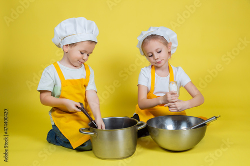 kids in apron and chef's hat sitting on the floor with a bowl and whisk