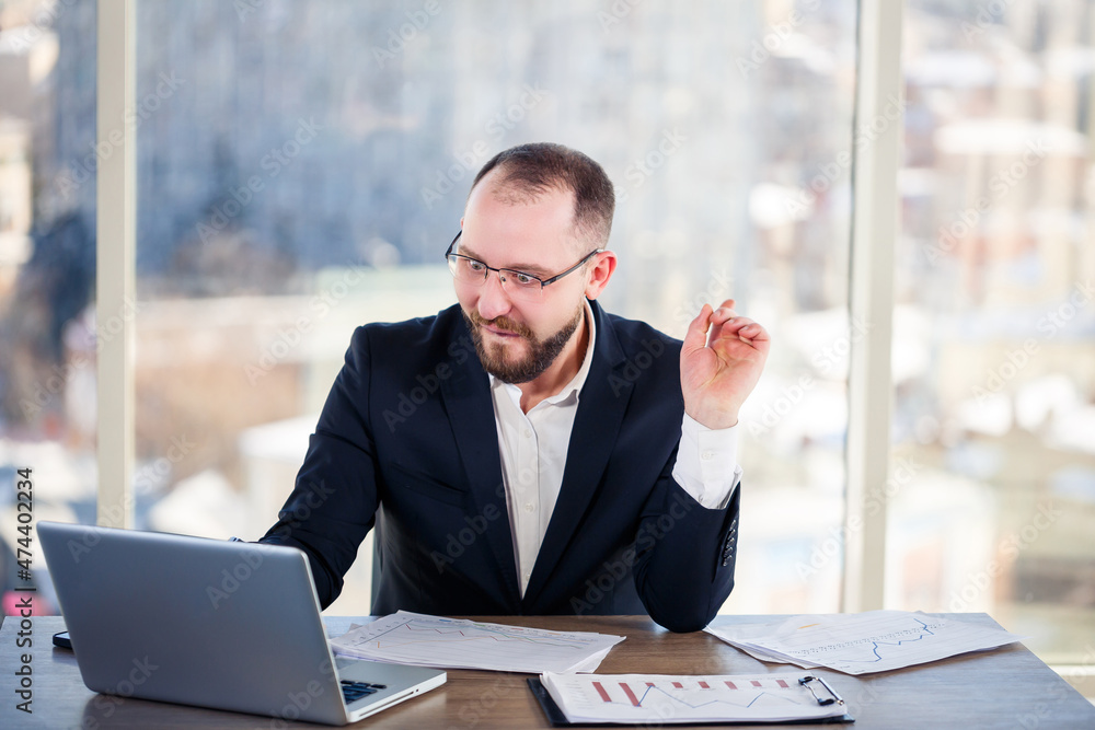 The corporate madman is sitting at the computer in the office and going crazy, the emotional portrait of the man at the table. Crazy worker at his workplace The corporate madman is sitting at the computer in the office and going crazy, the emotional portrait of the man at the table. Crazy worker at his workplace