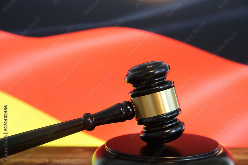 Closeup of isolated judge wood gavel with blurred german flag background (focus on hammer head)