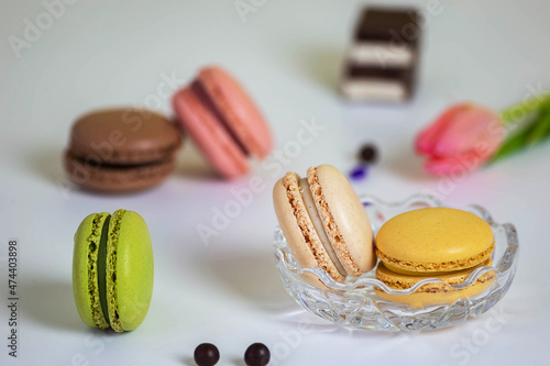 Macarons di colore diverso in piattino di vetro sul tavolo bianco decorato con palline verdi e cioccolatini con doppio strato in fondo photo