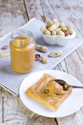 Peanut butter in a glass jar with a napkin on a wooden background. Delicious and healthy breakfast.