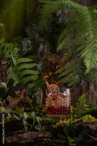 Cocktail with red syrup,tonic water,orange and cinnamon on the forest with fire and smoke.
