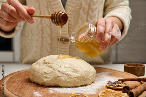 Close-up woman preparing gingerbread dough, holding a wooden stick and pouring some honey on pastry