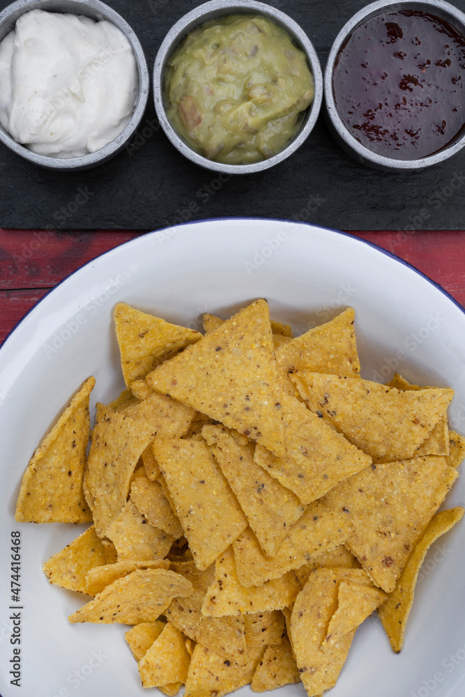 Mexican food. Top view of nachos in a white bowl and three dipping sauces of cheddar cheese, sweet chili and guacamole. Mexican food. Top view of nachos in a white bowl and three dipping sauces of cheddar cheese, sweet chili and guacamole.