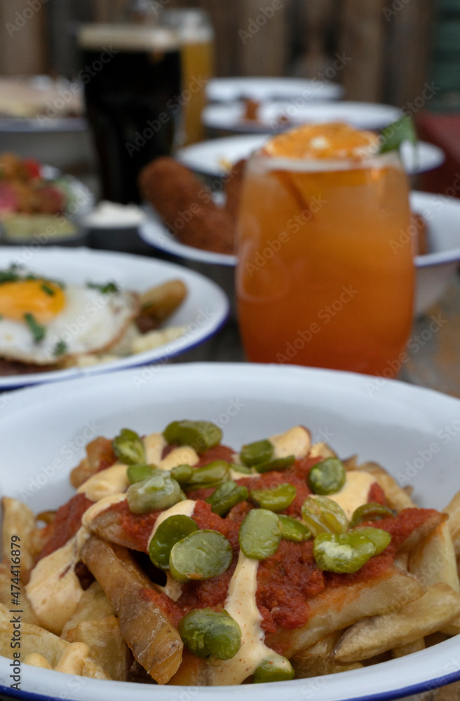 Ready to eat. View of french fries with broad beans and spicy sauces at the restaurant table. Other dishes, beer and tropical cocktails in the background. Ready to eat. View of french fries with broad beans and spicy sauces at the restaurant table. Other dishes, beer and tropical cocktails in the background.