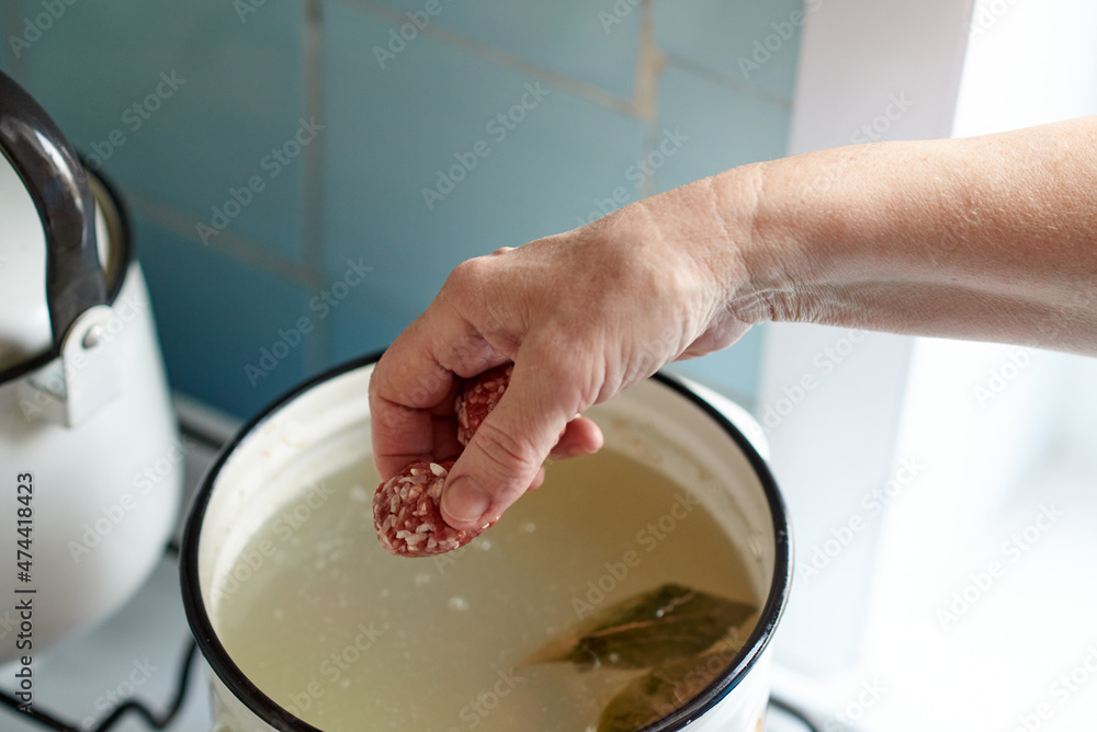 A woman's hand tosses a meatball into a pot of boiling soup. Healthy home cooking. A woman's hand tosses a meatball into a pot of boiling soup. Healthy home cooking.