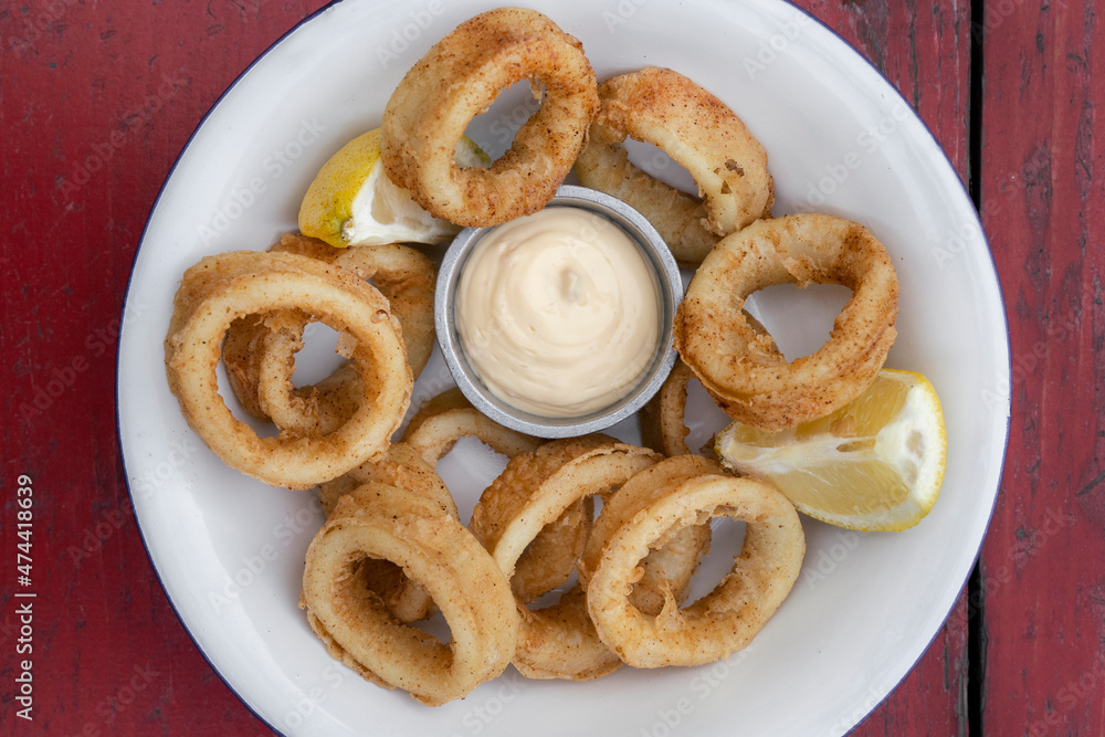 Deep fried seafood. Top view of delicious fried squid rings with lemon and a dipping sauce in a white bowl. Deep fried seafood. Top view of delicious fried squid rings with lemon and a dipping sauce in a white bowl.