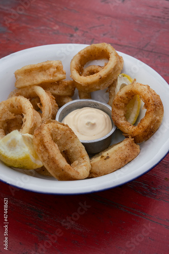 Seafood. Closeup view of fried squid rings with lemon and a dipping sauce, in a white bowl on the wooden table. 
