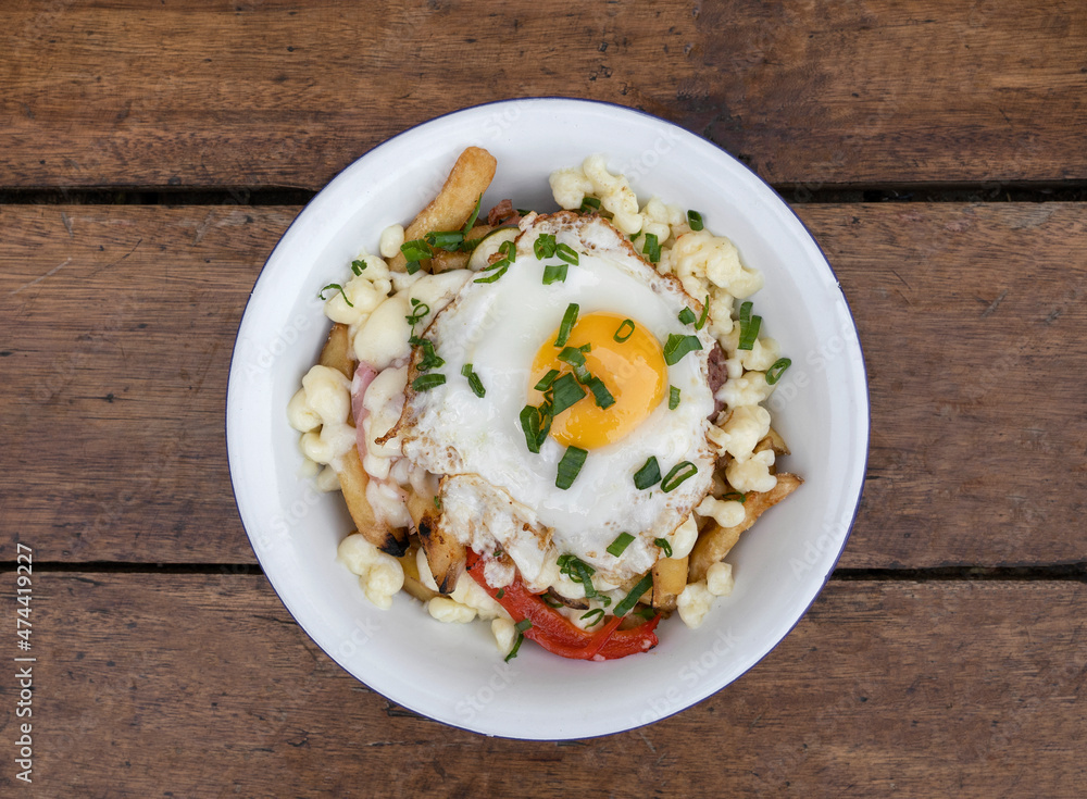 Top view of fried potatoes with melted cheese, chorizo, bell pepper, onion and a grilled egg in a white bowl on the wooden table. Top view of fried potatoes with melted cheese, chorizo, bell pepper, onion and a grilled egg in a white bowl on the wooden table.