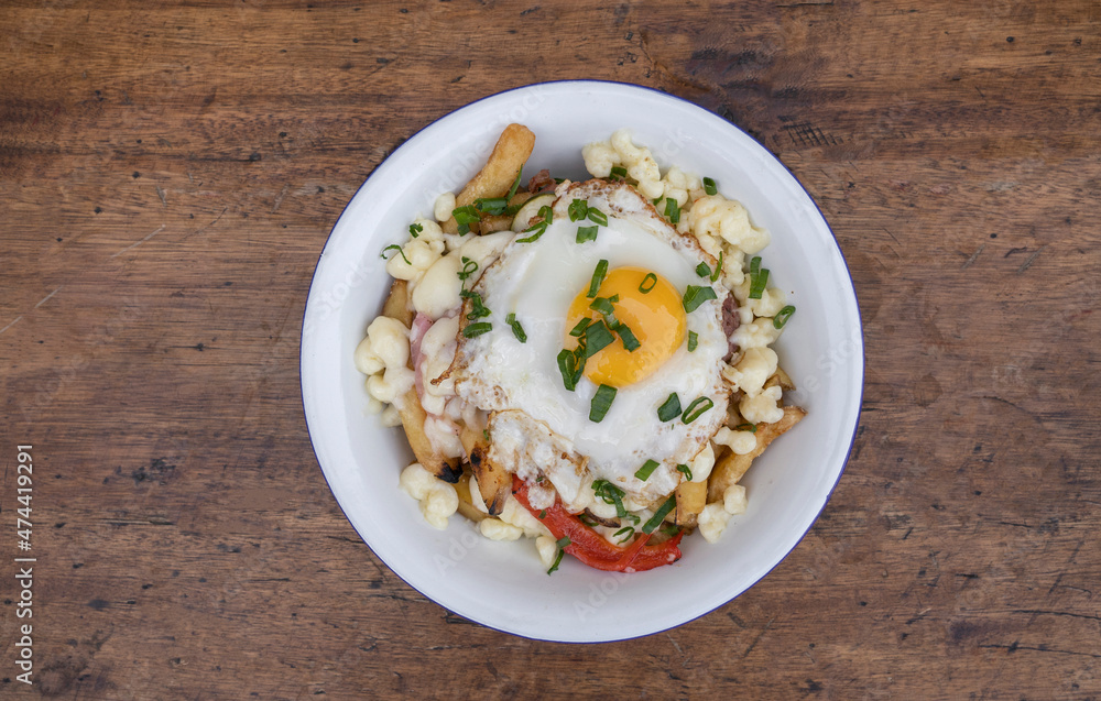 Top view of fried potatoes with melted cheese, chorizo, bell pepper, onion and a grilled egg in a white bowl on the wooden table. Top view of fried potatoes with melted cheese, chorizo, bell pepper, onion and a grilled egg in a white bowl on the wooden table.