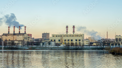 Smoking chimneys of thermal power plants near the waterfront in city. Winter. Industrial and nature background.