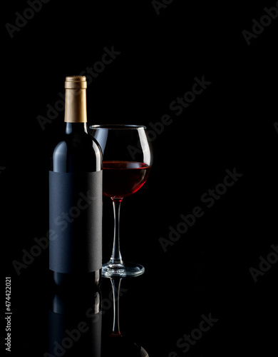 bottle and glass of red wine on a dark background with reflection