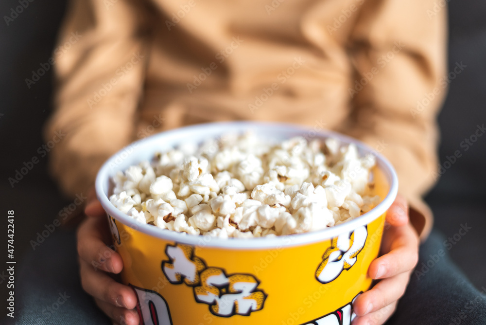 From above of crop unrecognizable person sitting on sofa with bucket full of yummy popcorn From above of crop unrecognizable person sitting on sofa with bucket full of yummy popcorn