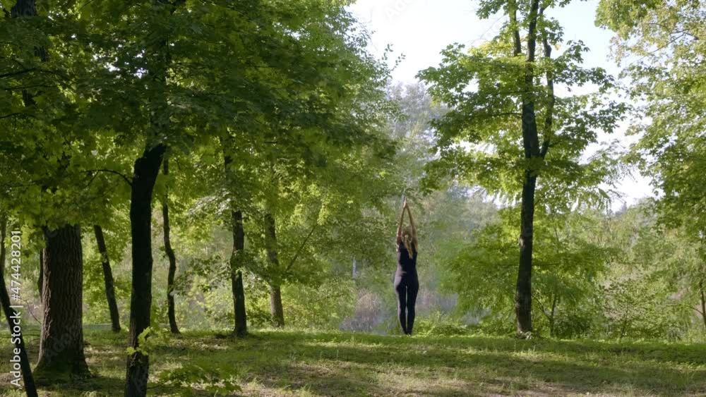 Silhouette woman raising arms in air. Woman practices yoga at sunrise in forest. Woman performing a spiritual yoga pose. Concept of fitness, healthy lifestyle Silhouette woman raising arms in air. Woman practices yoga at sunrise in forest. Woman performing a spiritual yoga pose. Concept of fitness, healthy lifestyle
