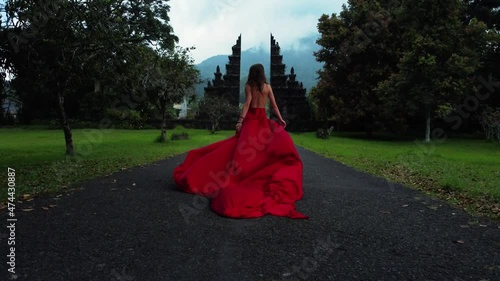 Pretty asian woman walks to balinese gates in long red dress and drone follows in slowmotion on Hangara gates in Bali Indonesia. fashion concept. High quality fullhd aerial footage