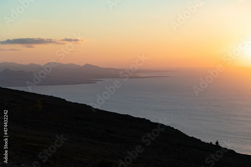 Silueta de dos jóvenes sentados con luz de atardecer y una isla en el océano al fondo