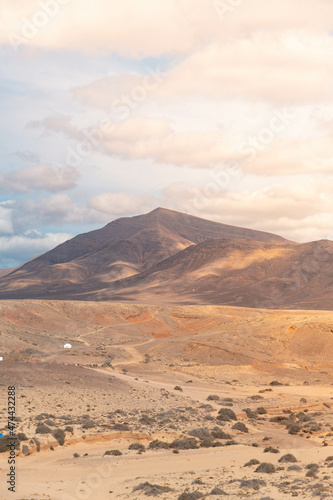 Paisaje vertical anaranjado de una paisaje volcánico y rocoso. Cielo niblado y una montaña al fono. (Lanzarote, Islas Canarias, España)