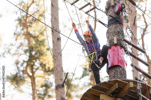 the girl in the orange helmet in the adventure Park holds on to the ropes